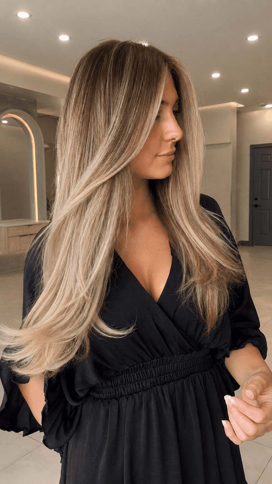 Long-haired woman in black dress, standing indoors with modern decor.