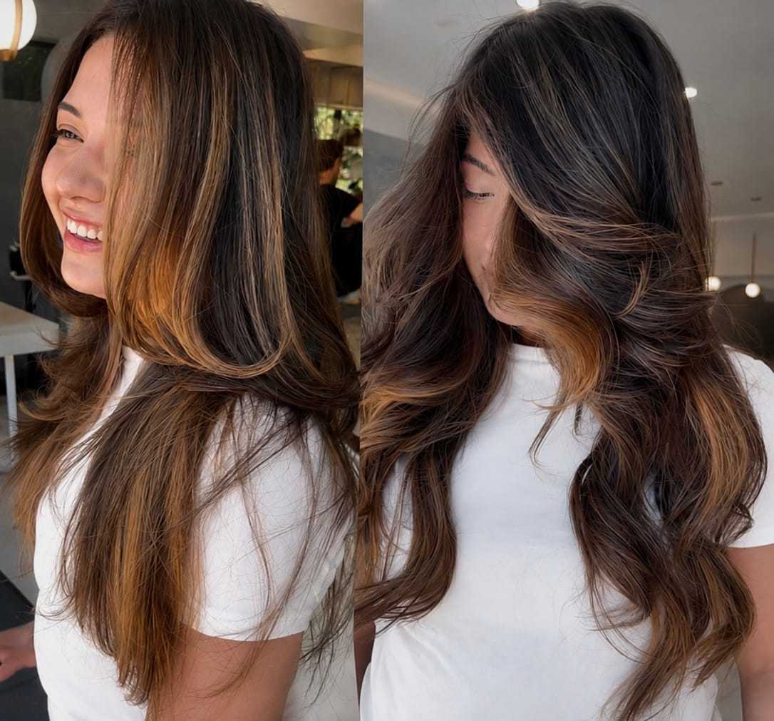 Woman with long, wavy hair and caramel highlights in a salon. Bright, welcoming smile.