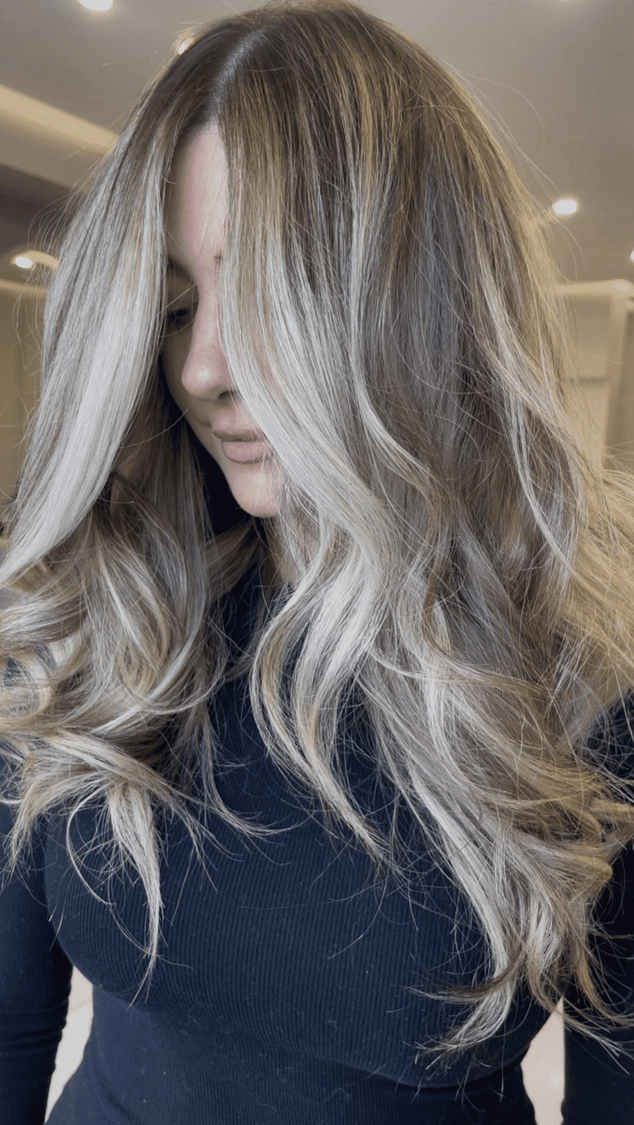 Long, wavy blonde hair with dark roots, styled in a salon setting.